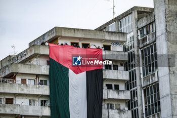 2023-10-18 - A large flag of about 30 metres with the colours of Palestine was displayed for a few minutes on the Vele in Scampia, at the initiative of activists of the Network for Palestine. About forty activists were present. The flag was displayed for a few minutes and then removed, attracting the attention of passers-by. - NAPLES, PRO-PALESTINE DEMONSTRATORS IN SCAMPIA - NEWS - CHRONICLE