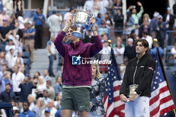 2024-09-08 - Winner Jannik Sinner of Italy celebrates while Taylor Fritz of USA looks on during the trophy ceremony of the men's final on day 14 of the 2024 US Open, Grand Slam tennis tournament on September 8, 2024 at USTA Billie Jean King National Tennis Center in Flushing Meadows, Queens, New York, United States - TENNIS - US OPEN 2024 - 08/09 - INTERNATIONALS - TENNIS