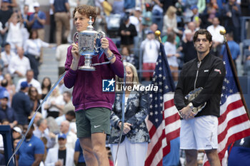 2024-09-08 - Winner Jannik Sinner of Italy celebrates while Taylor Fritz of USA looks on during the trophy ceremony of the men's final on day 14 of the 2024 US Open, Grand Slam tennis tournament on September 8, 2024 at USTA Billie Jean King National Tennis Center in Flushing Meadows, Queens, New York, United States - TENNIS - US OPEN 2024 - 08/09 - INTERNATIONALS - TENNIS